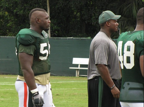 Senior defensive tackle Micanor Regis unveils his new haircut during practice while Marcus Forston helps coach his defensive teammates.