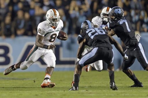 Miami's Duke Johnson (8) runs the ball as North Carolina's Dominique Green (26) and Tim Scott (7) move in to attempt the tackle during the first half...