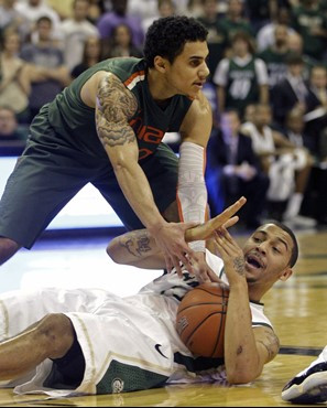 Charlotte's Pierria Henry, bottom, tries to call a time-out as Miami's Shane Larkin, top, closes in during the first half of an NCAA college...
