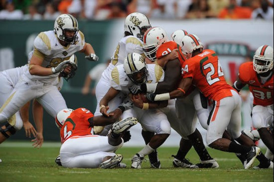 University of Miami Hurricanes defenders Chavez Grant #24, linebacker Marcus Robinson #56, and defensive tackle Joe Joseph #91 make a gang tackle...